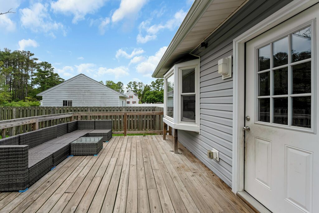 A deck with outdoor furniture, a wooden fence, and a house with a white door.