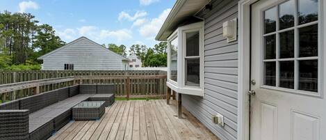 A deck with outdoor furniture, a wooden fence, and a house with a white door.