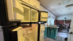 A compact kitchen with open refrigerator doors, a sink, and teal cabinets. - 2-bedroom RV in fantastic Clearwater with AC and some equipments for fitness (Clearwater)