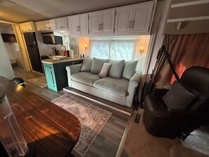Interior compacto de una caravana con kitchenette, un sofá, una mesa de comedor y una silla.