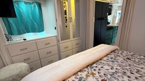 A bedroom with a bed, a vanity with a mirror, and a kitchenette in the background. - 2-bedroom RV in fantastic Clearwater with AC and some equipments for fitness (Clearwater)