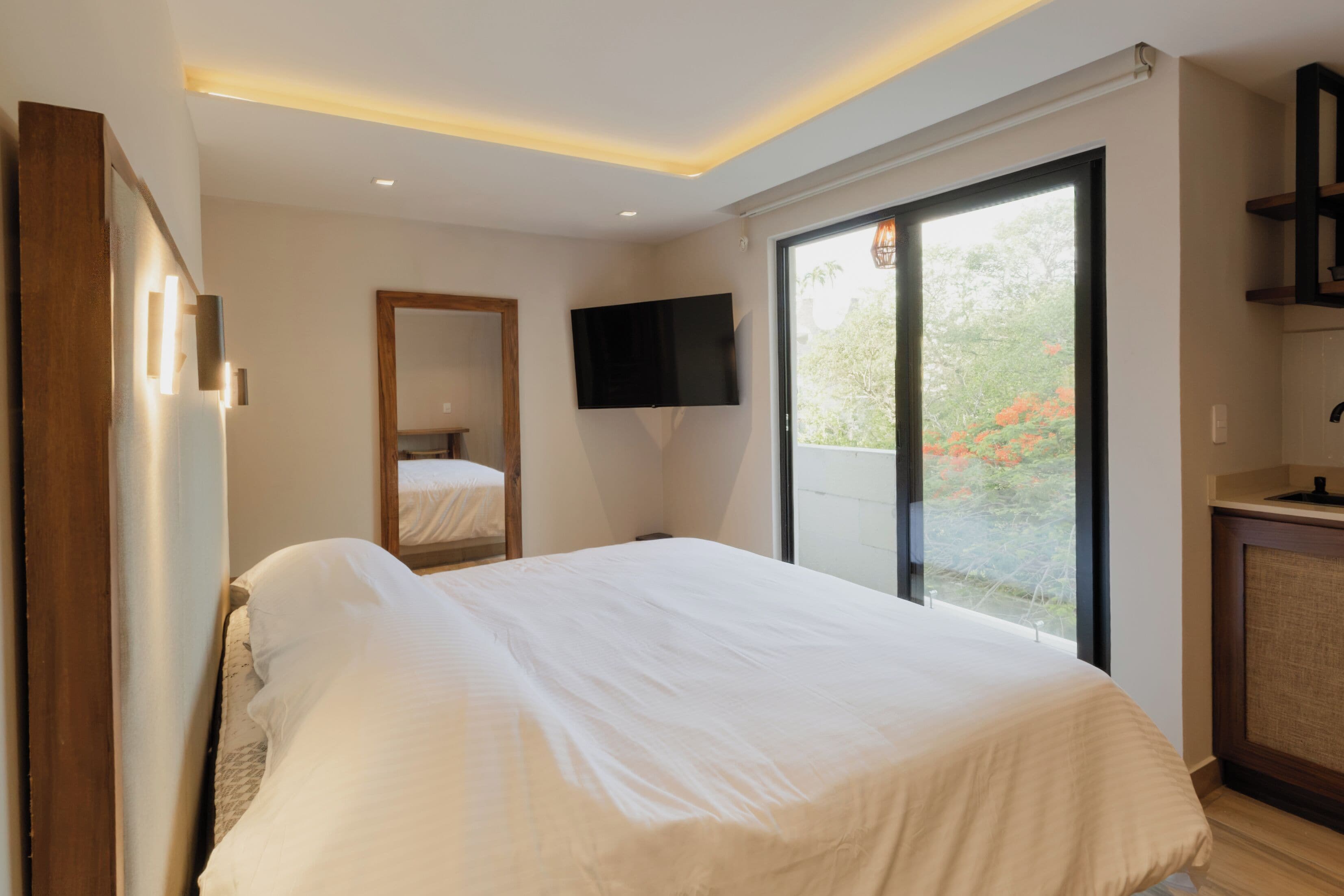 Une chambre moderne dotée d’un grand lit, d’un téléviseur à écran plat et d’une porte-fenêtre coulissante donnant sur un balcon.
