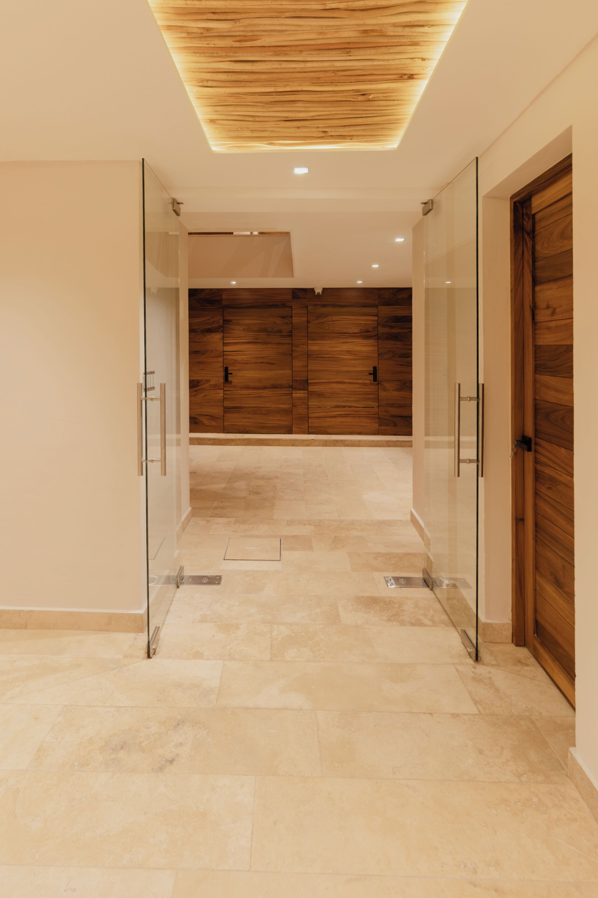 A hallway with glass doors, wooden cabinets, and a tiled floor.