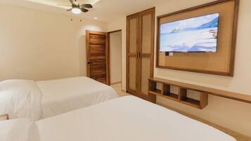 Habitación de hotel con dos camas, un televisor montado en la pared, ventilador de techo y puertas de armario de madera.