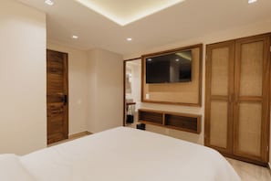 A bedroom with a bed, a TV mounted on the wall, wooden wardrobe, and a ceiling light. - Nidara Suites (Playa del Carmen)