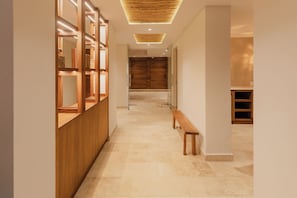 A hallway with a wooden bench, a wooden reception desk, and a large wooden door at the end. - Nidara Suites (Playa del Carmen)