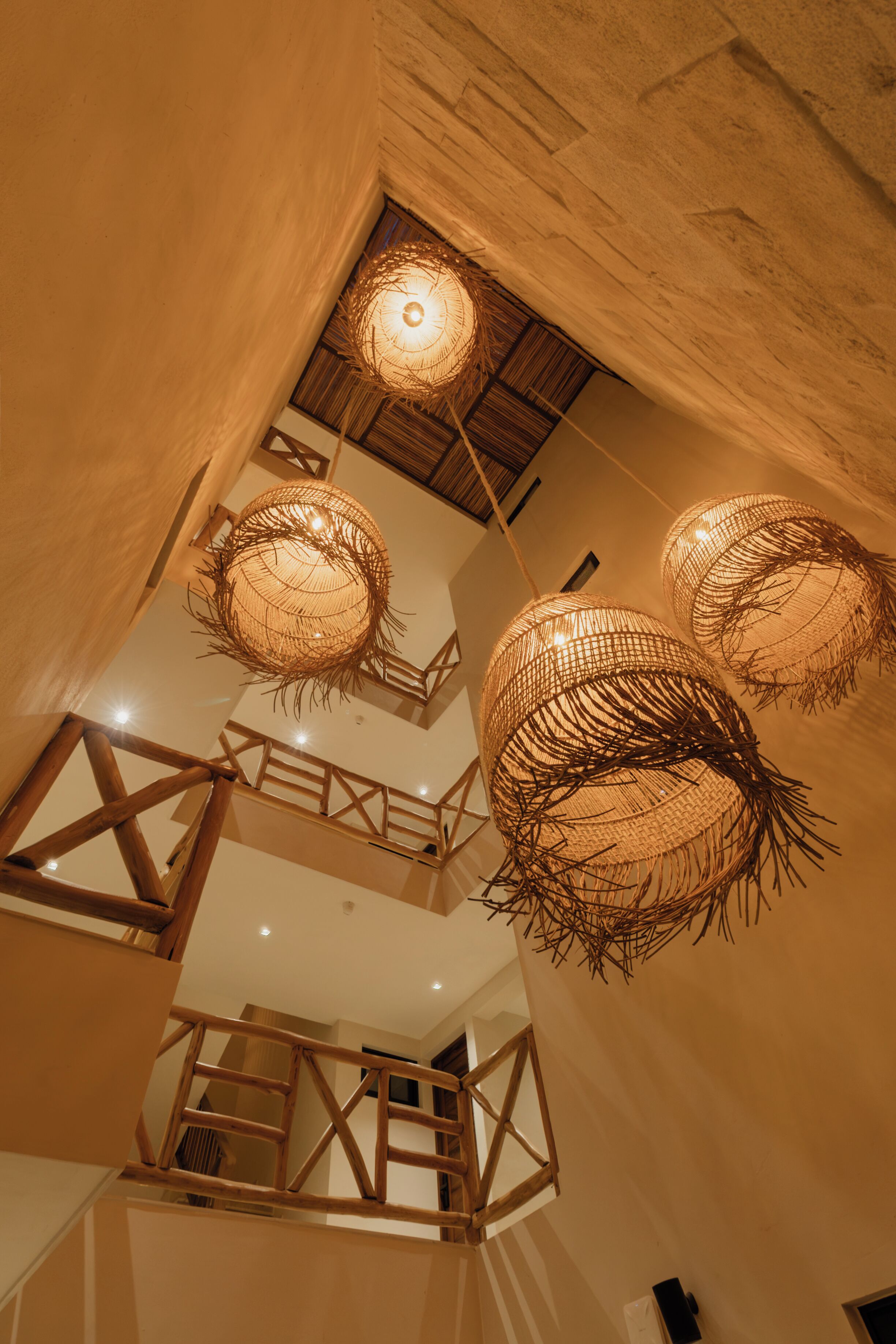 Ein mehrgeschossiges Interieur mit freiliegenden Holzbalken, einer Treppe und kugelförmigen, gewebten Leuchten.