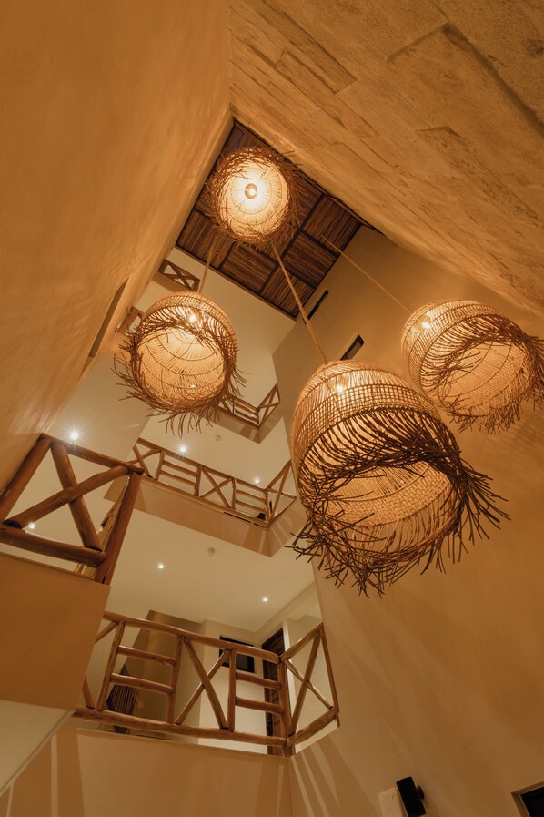Un interior de varios niveles con vigas de madera a la vista, una escalera y lámparas esféricas tejidas.