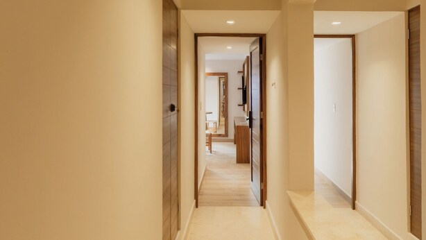 Un pasillo largo y estrecho con suelo de baldosas y puertas de madera a ambos lados.