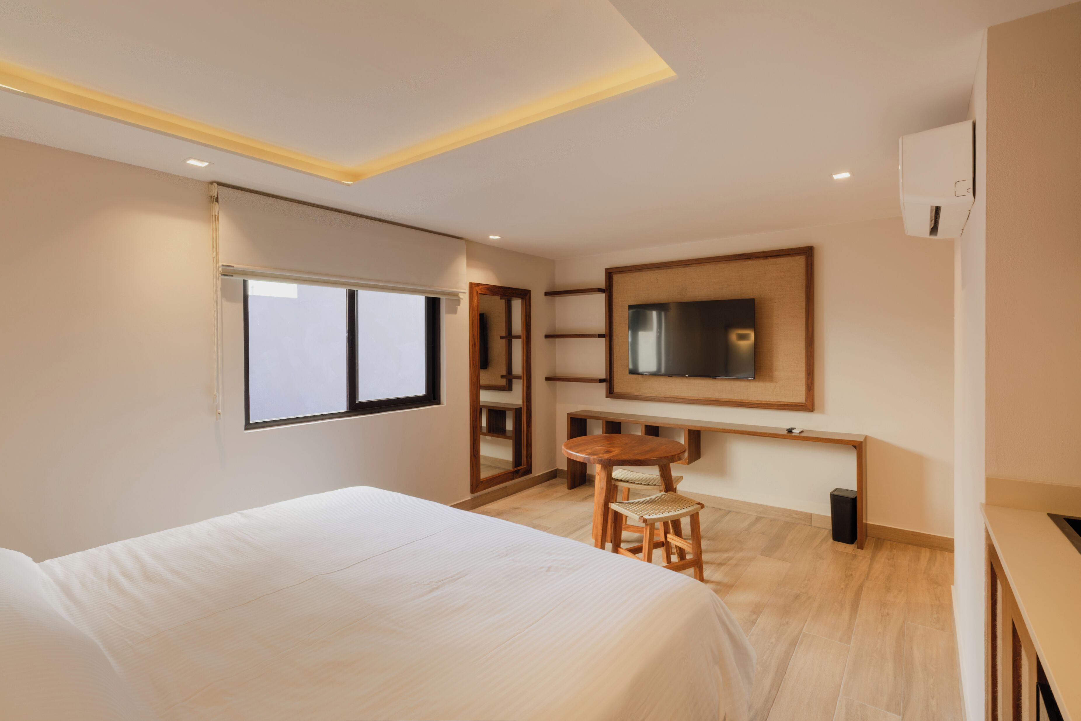 A hotel room with a bed, a small wooden table, a chair, a TV, and a mirror.