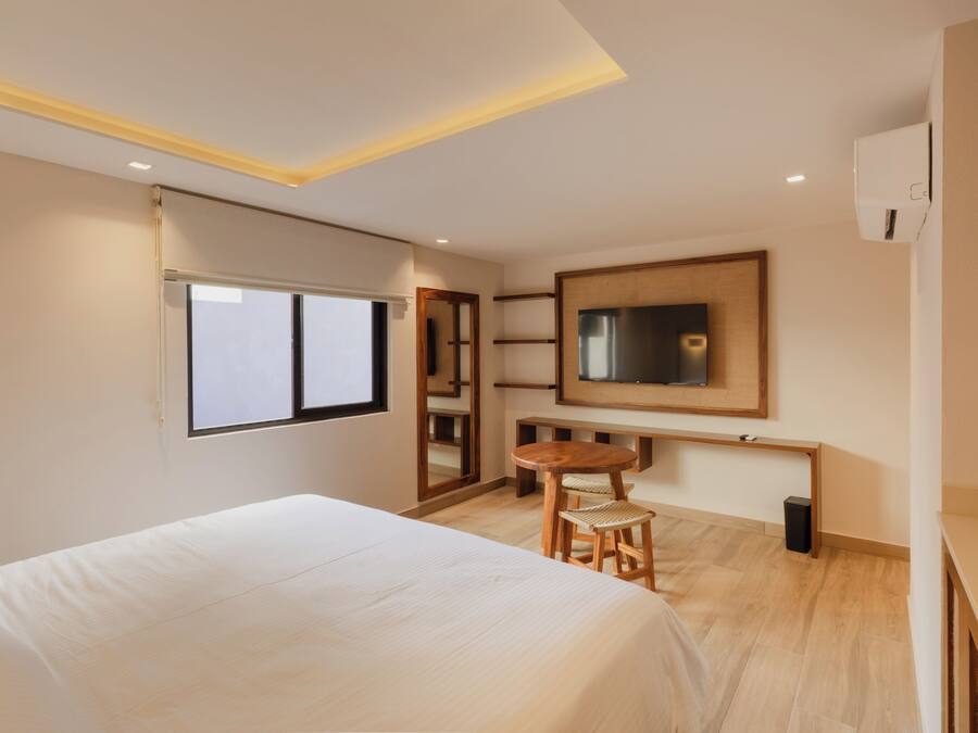 A hotel room with a bed, a small wooden table, a chair, a TV, and a mirror.