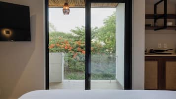 Une chambre avec un lit, un téléviseur fixé au mur et une porte coulissante donnant sur un balcon d’où l’on peut admirer les arbres et les fleurs.