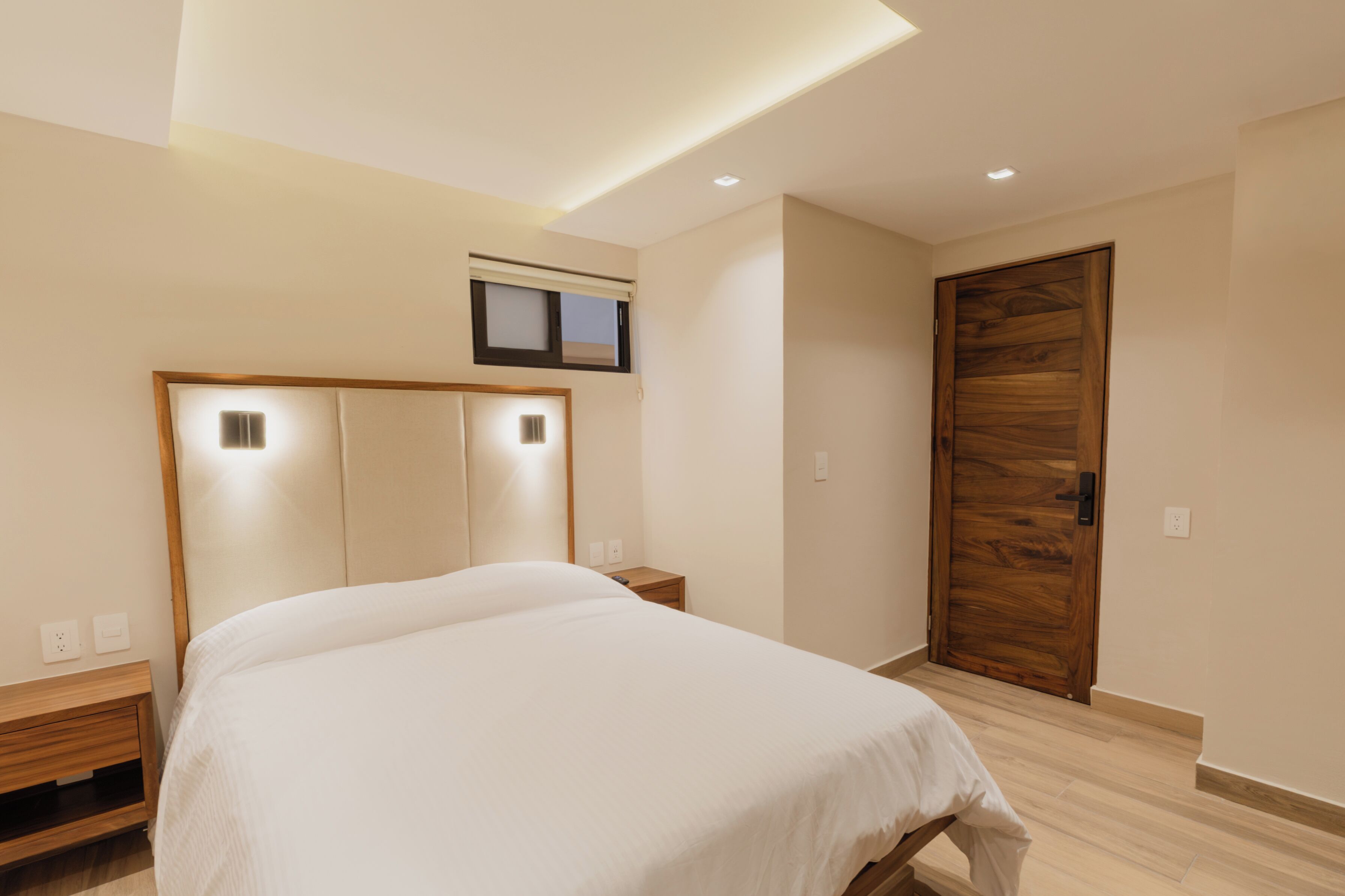Un dormitorio con cama, mesitas de noche, una puerta de madera y una lámpara en el techo.