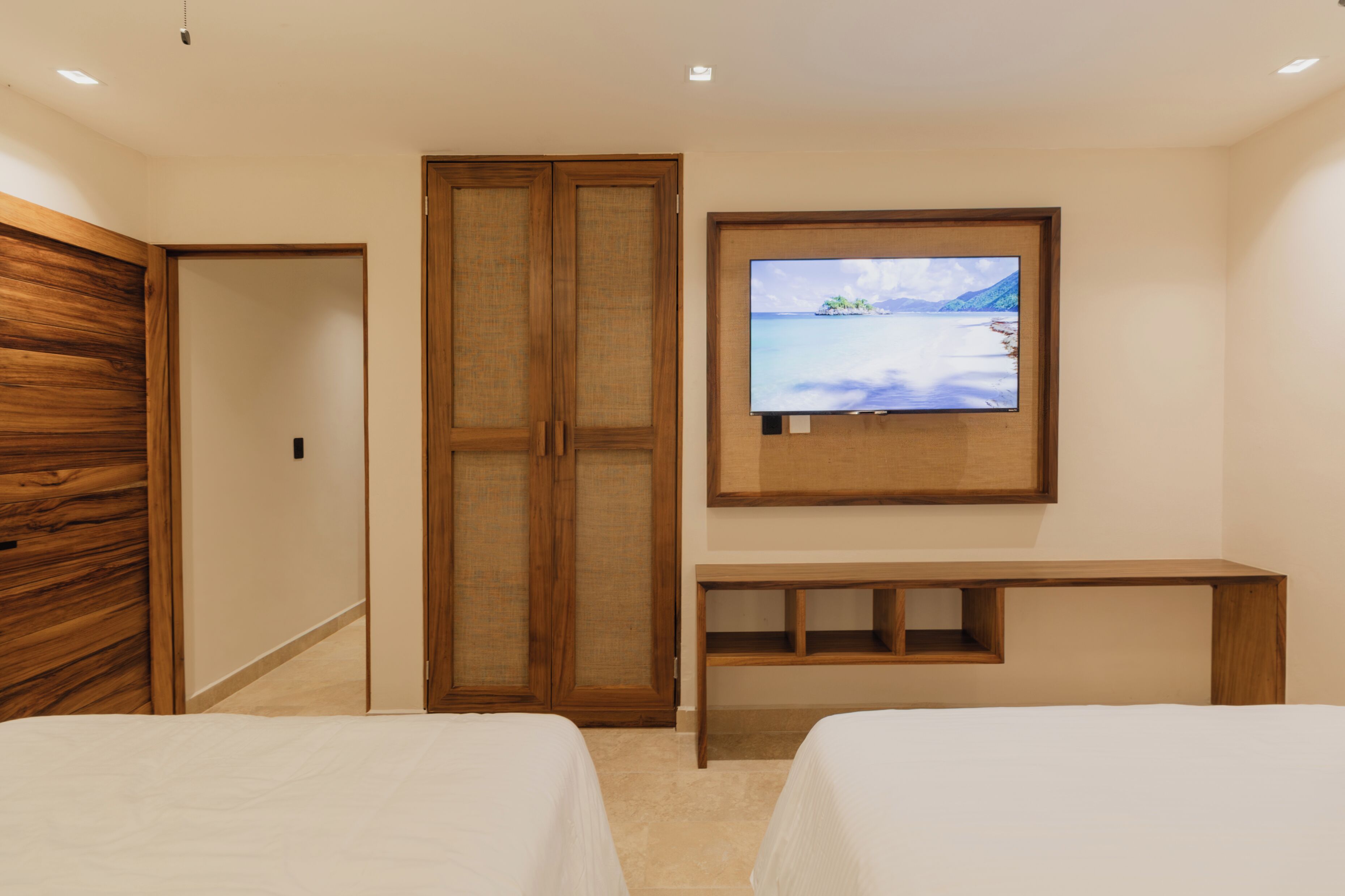 Una camera d'albergo con due letti, un armadio in legno, una televisione fissata al muro e una piccola scrivania in legno.