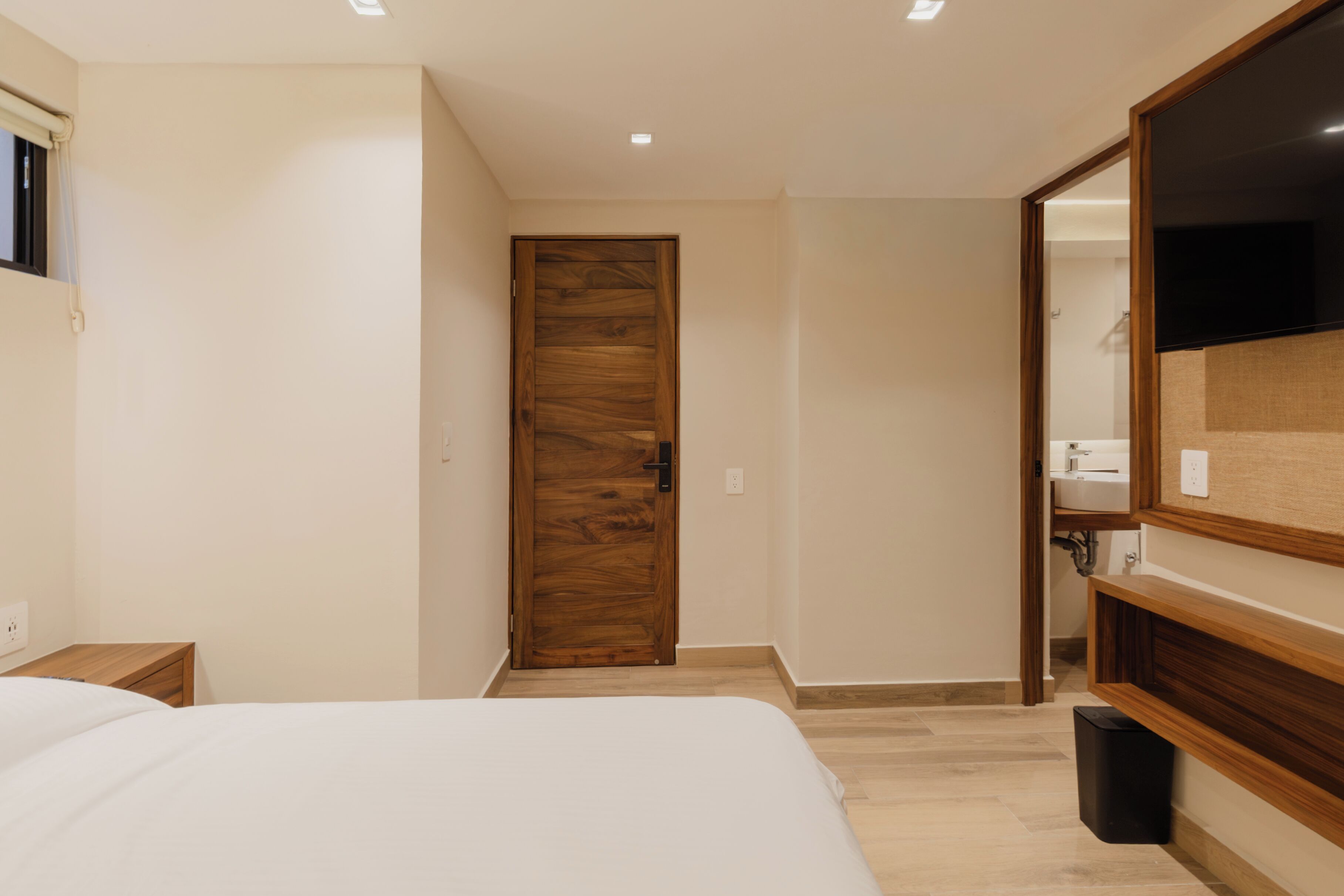 A bedroom with a wooden door, a bed, a mirror, and a small bedside table.