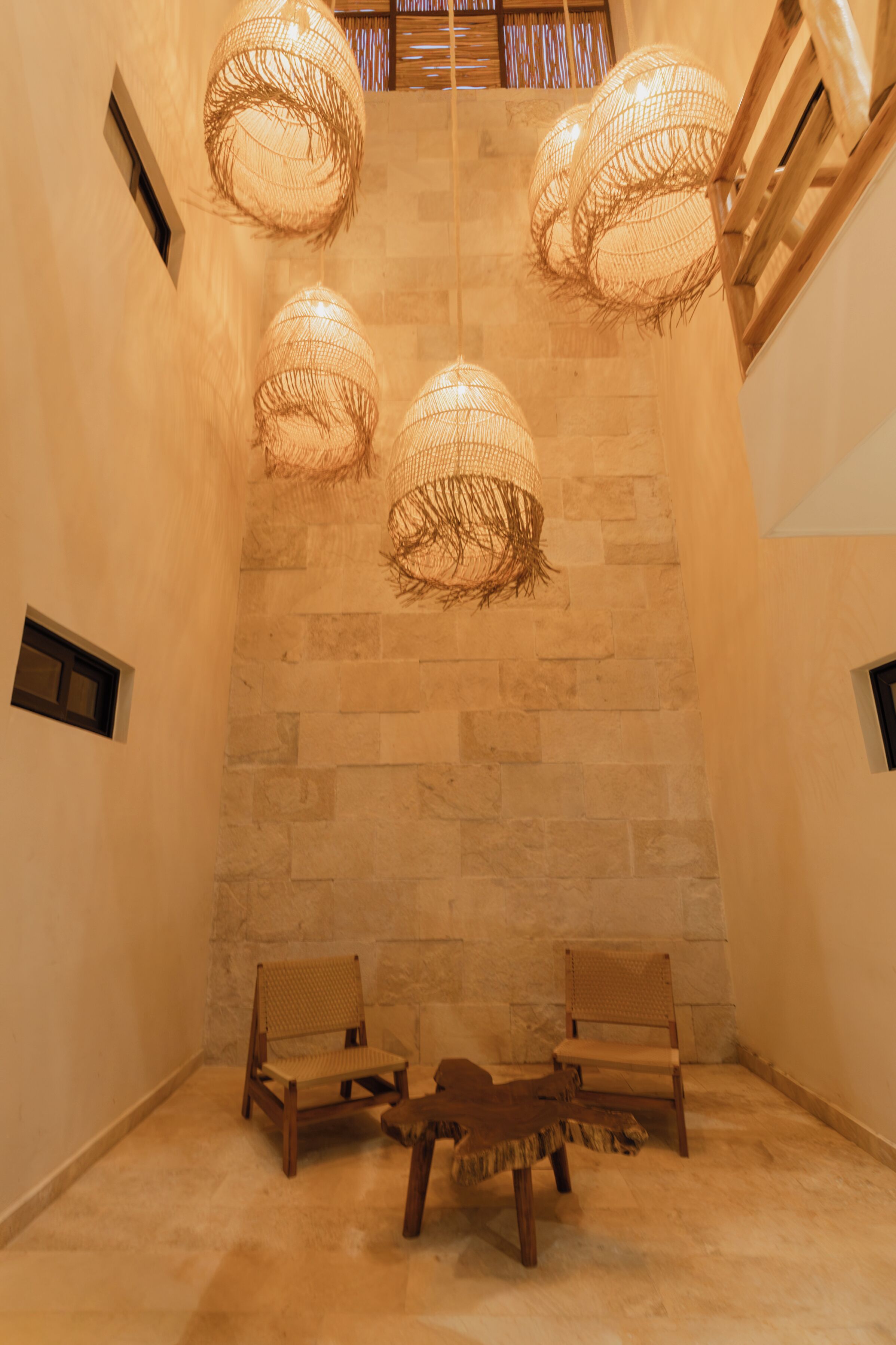 Una habitación con paredes de piedra, dos sillas de madera y tres lámparas de fibra.
