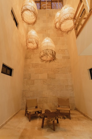 Um quarto com paredes de pedra, duas cadeiras de madeira e três luminárias de tecido.