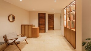 Un pasillo con mostrador de recepción, una silla, puertas de madera y un espejo en la pared.