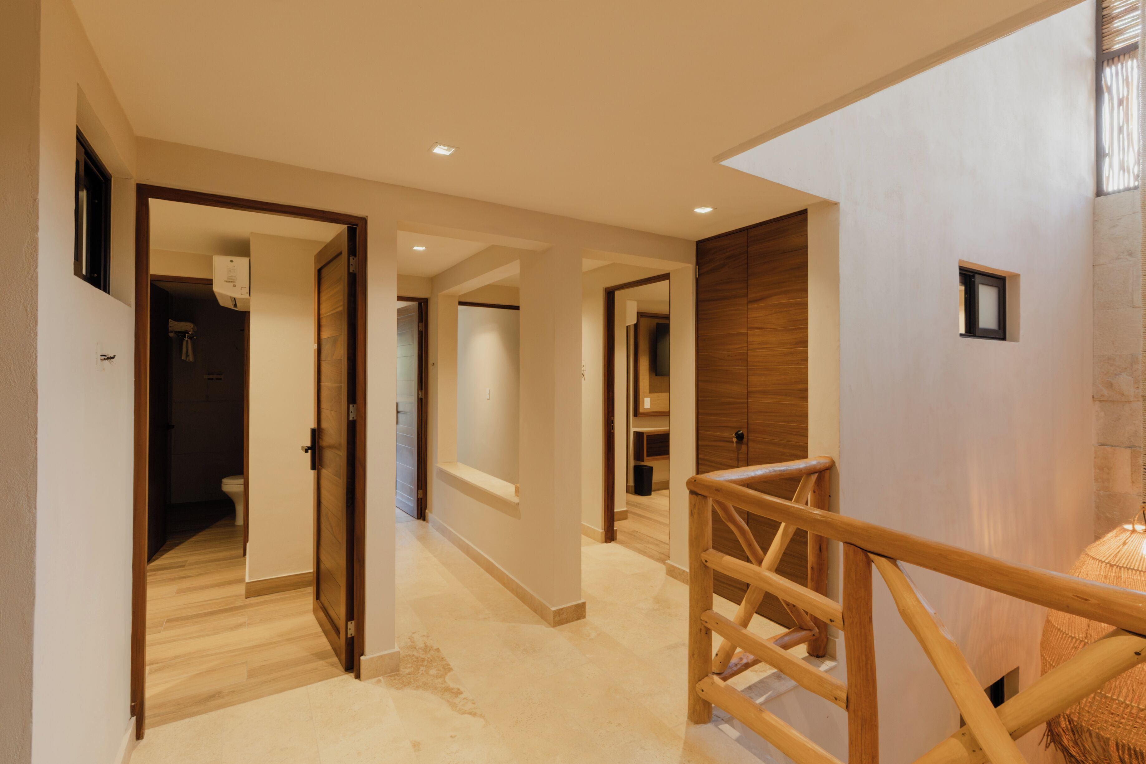 Un interior moderno con una escalera de madera, un pasillo que conduce a un baño y vista a una pared de piedra.