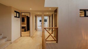 Un interior moderno con un pasillo que lleva a una escalera, barandas de madera y vistas a una habitación con televisor.