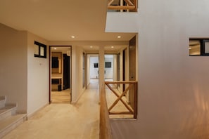 A modern interior with a hallway leading to a staircase, wooden railings, and a view into a room with a television. - Nidara Suites (Playa del Carmen)