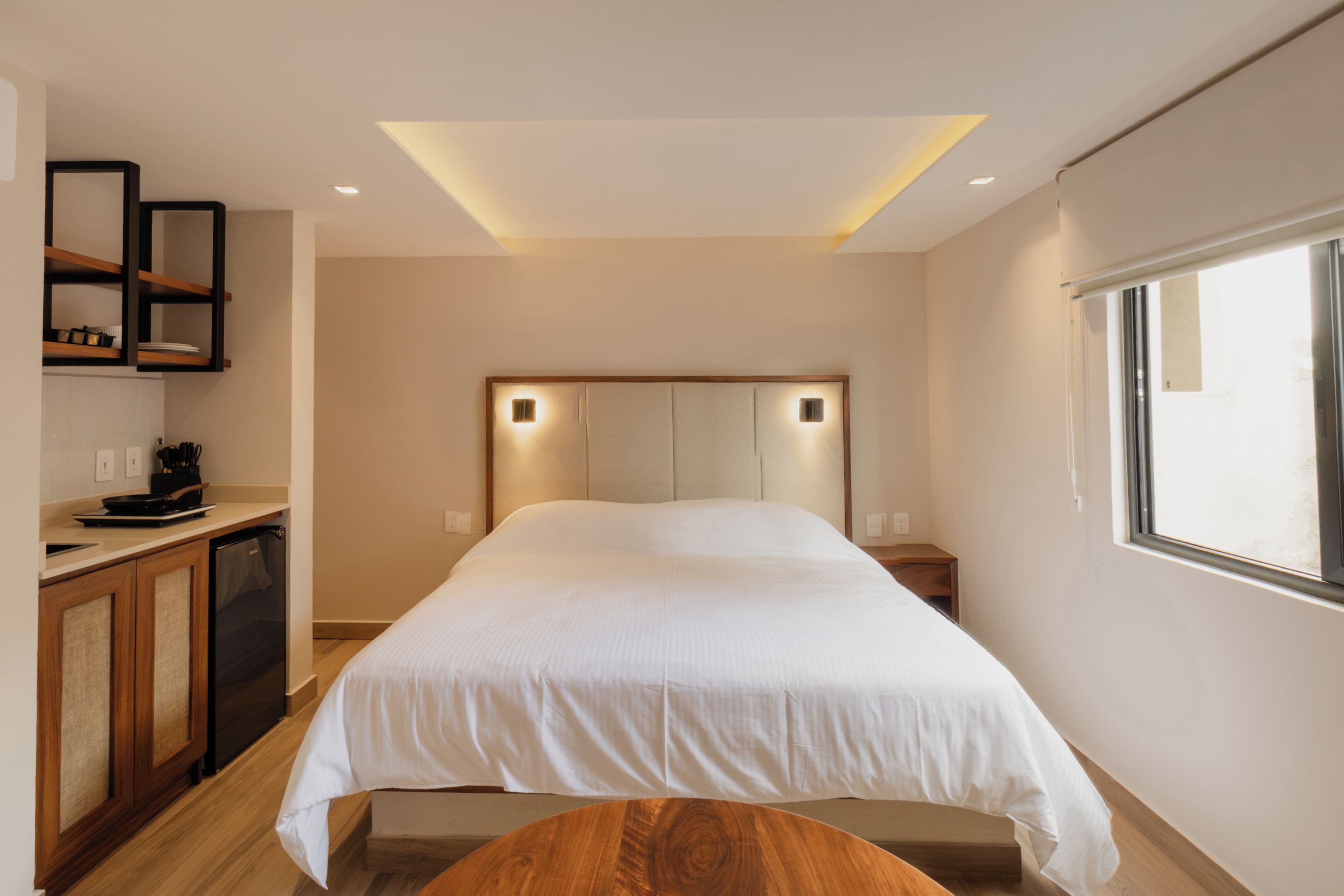 Un dormitorio con cama, mesitas de noche, un banco de madera, estantería empotrada y ventana.