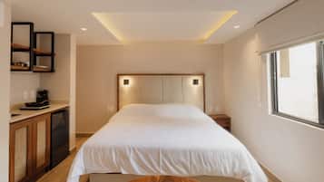 Un dormitorio con cama, mesitas de noche, un banco de madera, estantería empotrada y ventana.