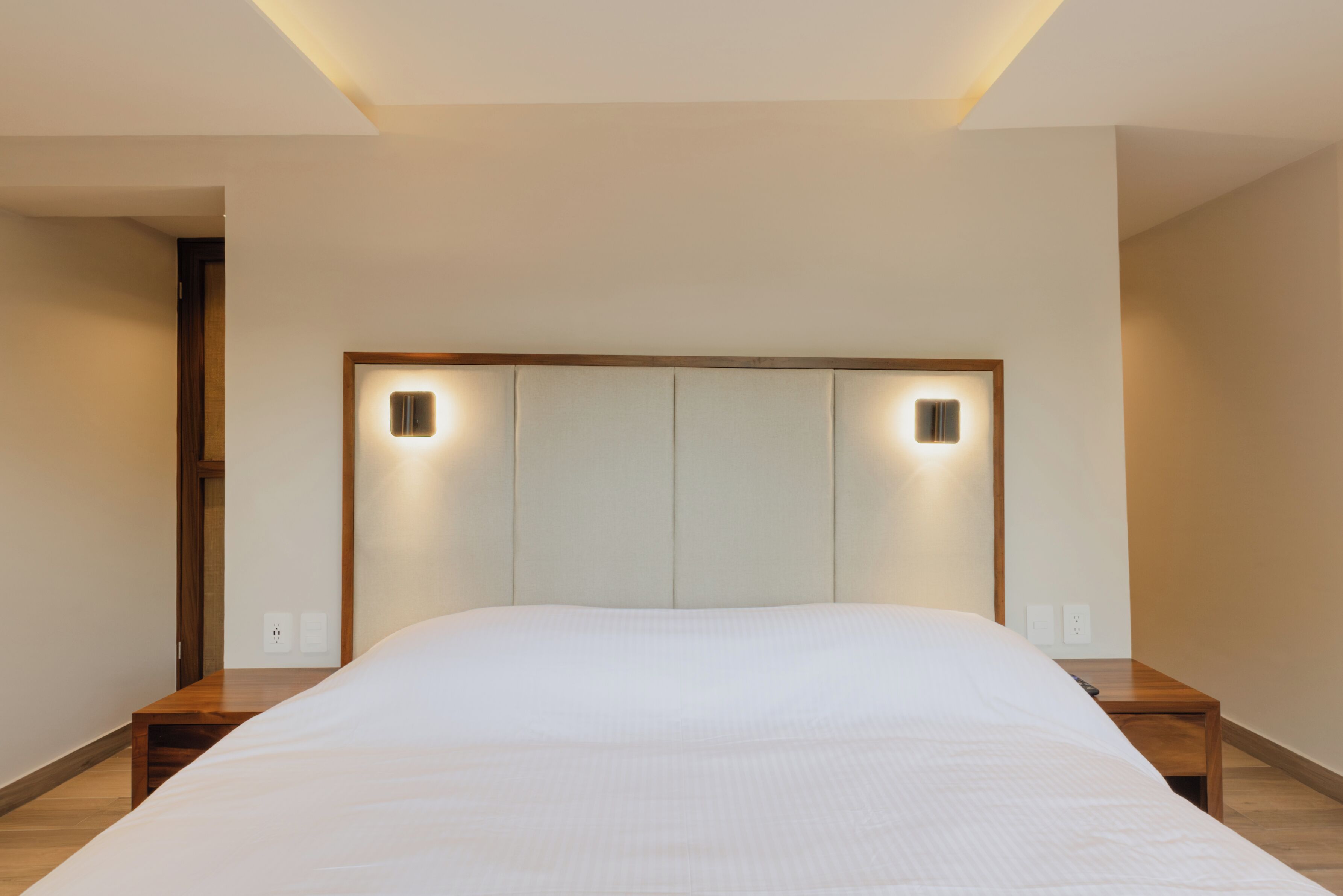 A modern bedroom with a large bed, wooden headboard, and bedside tables.