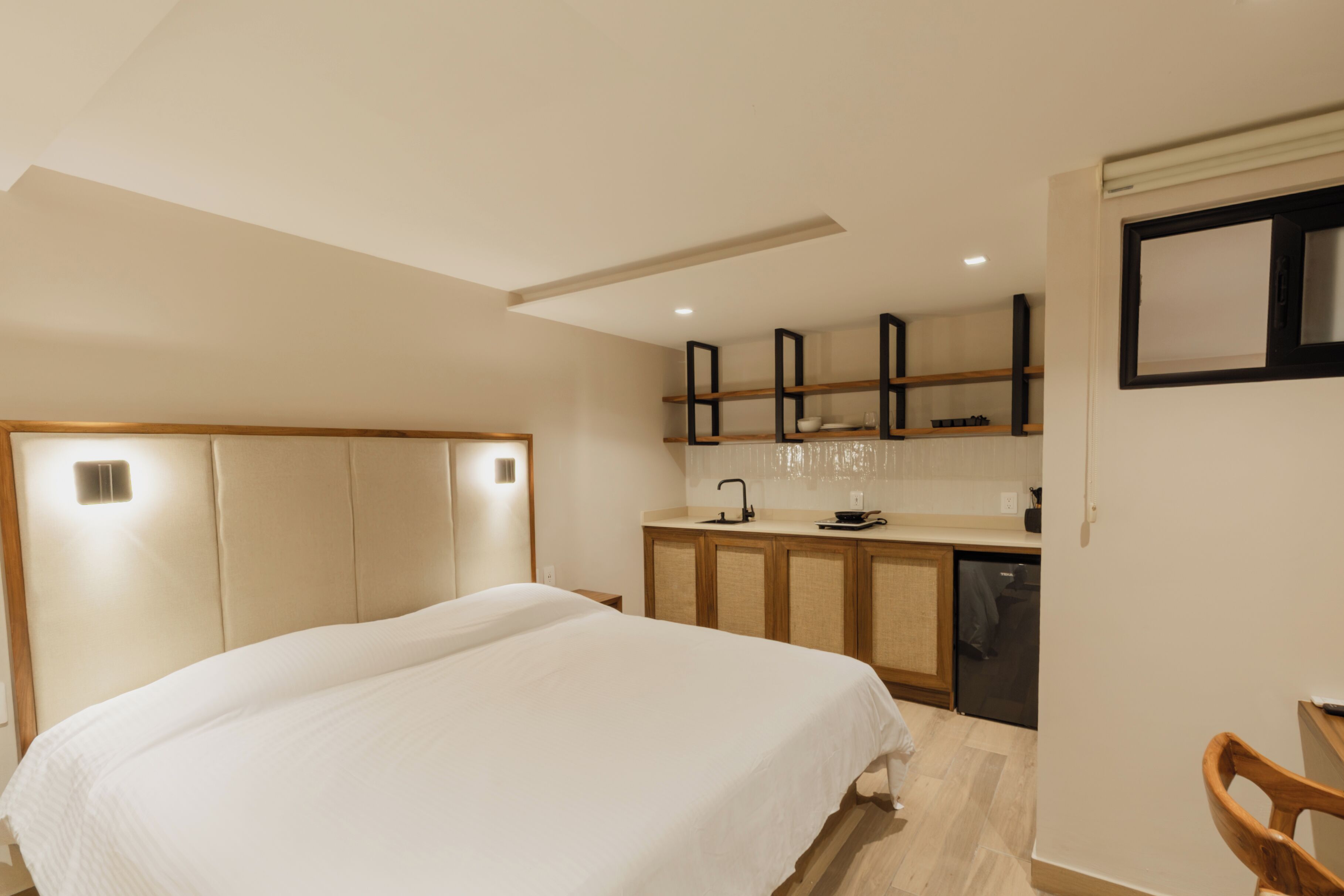 A hotel room with a bed, a small kitchenette, and a wooden chair.