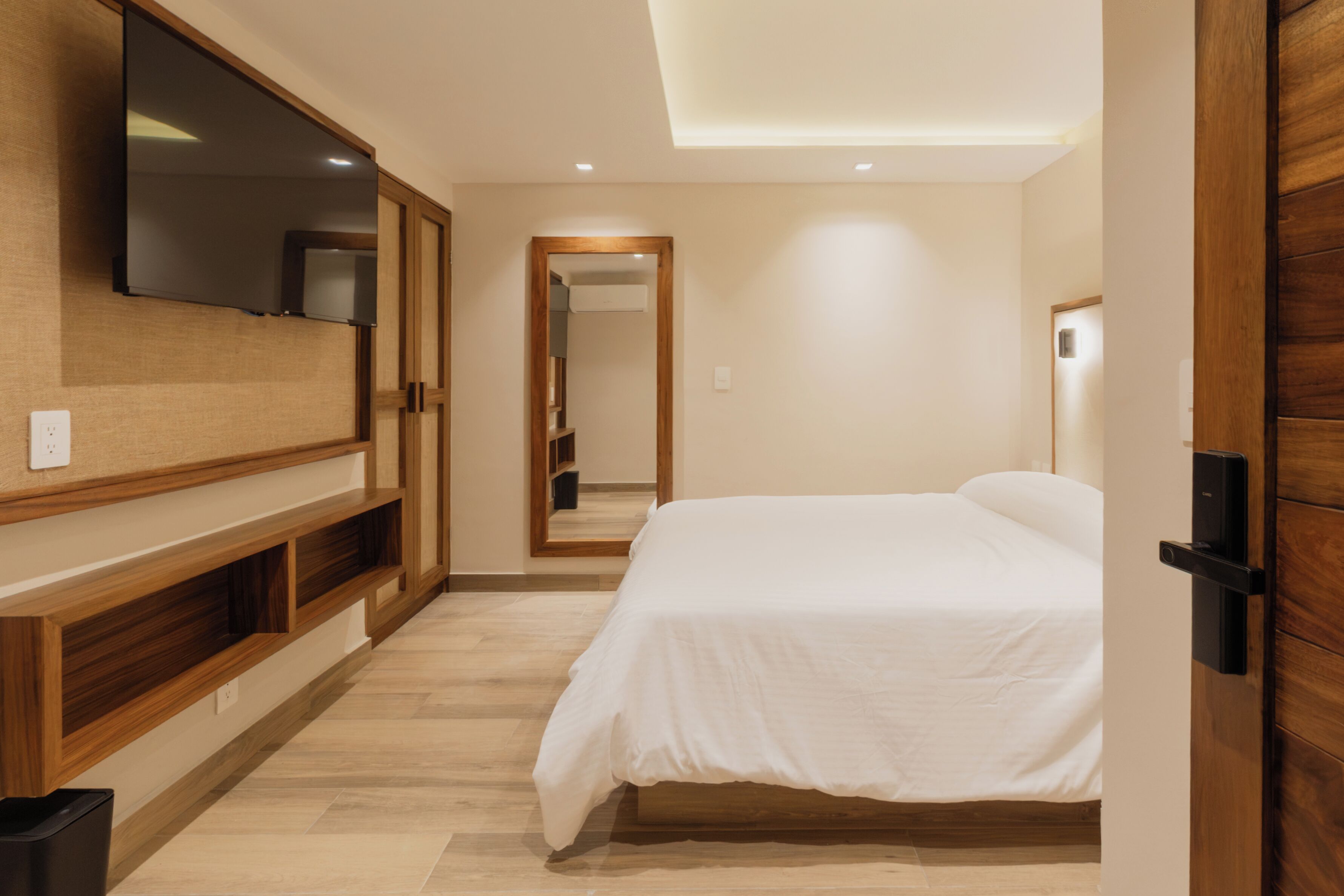 A bedroom with a bed, a TV mounted on the wall, and a wooden wardrobe.