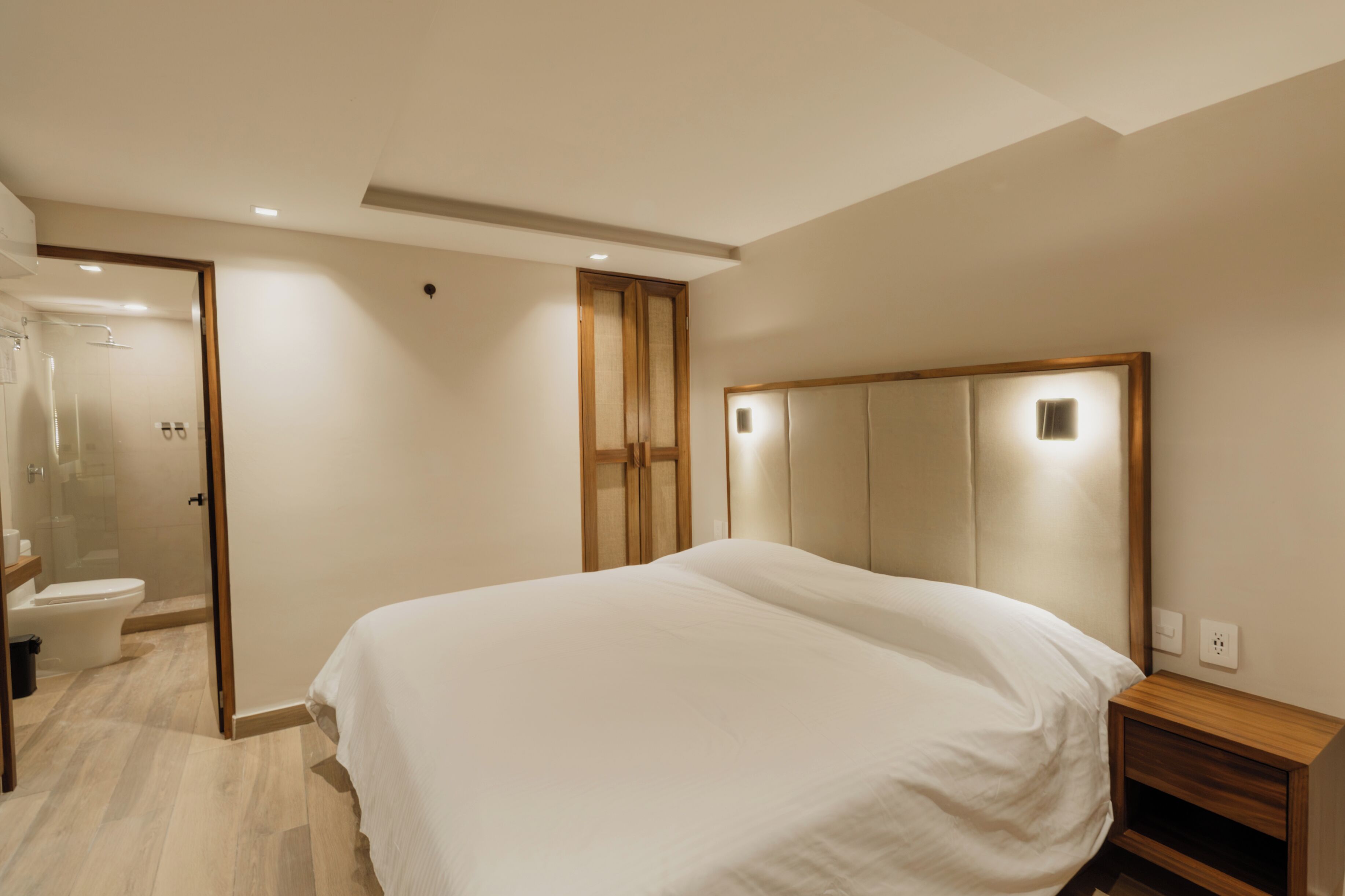 A bedroom with a large bed, a wooden nightstand, a mirror, and a shower area.