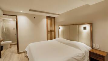 A bedroom with a large bed, a wooden nightstand, a mirror, and a shower area.