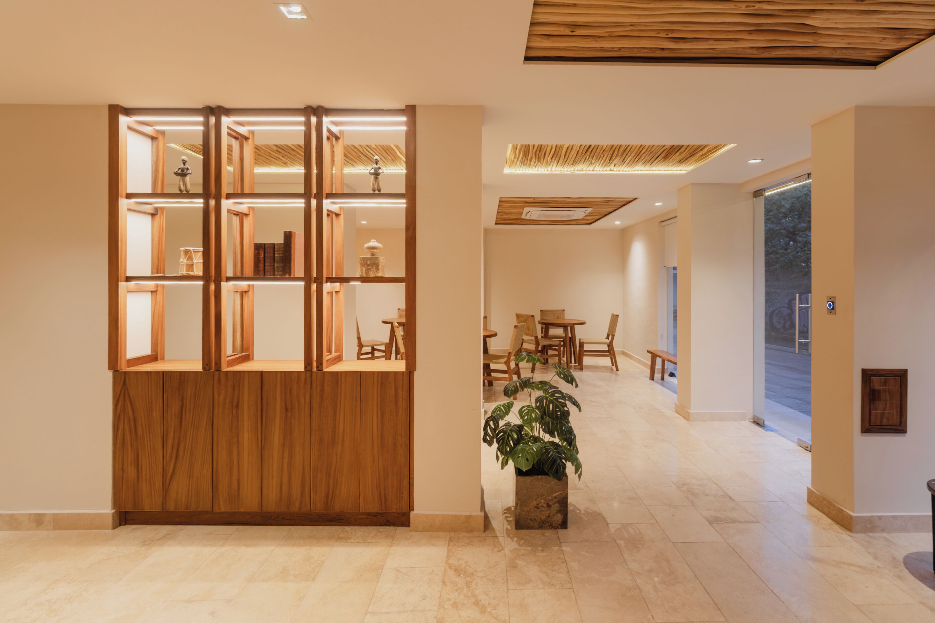 Un interior moderno con un separador de madera, una zona de comedor con sillas y mesas, y una planta en maceta.