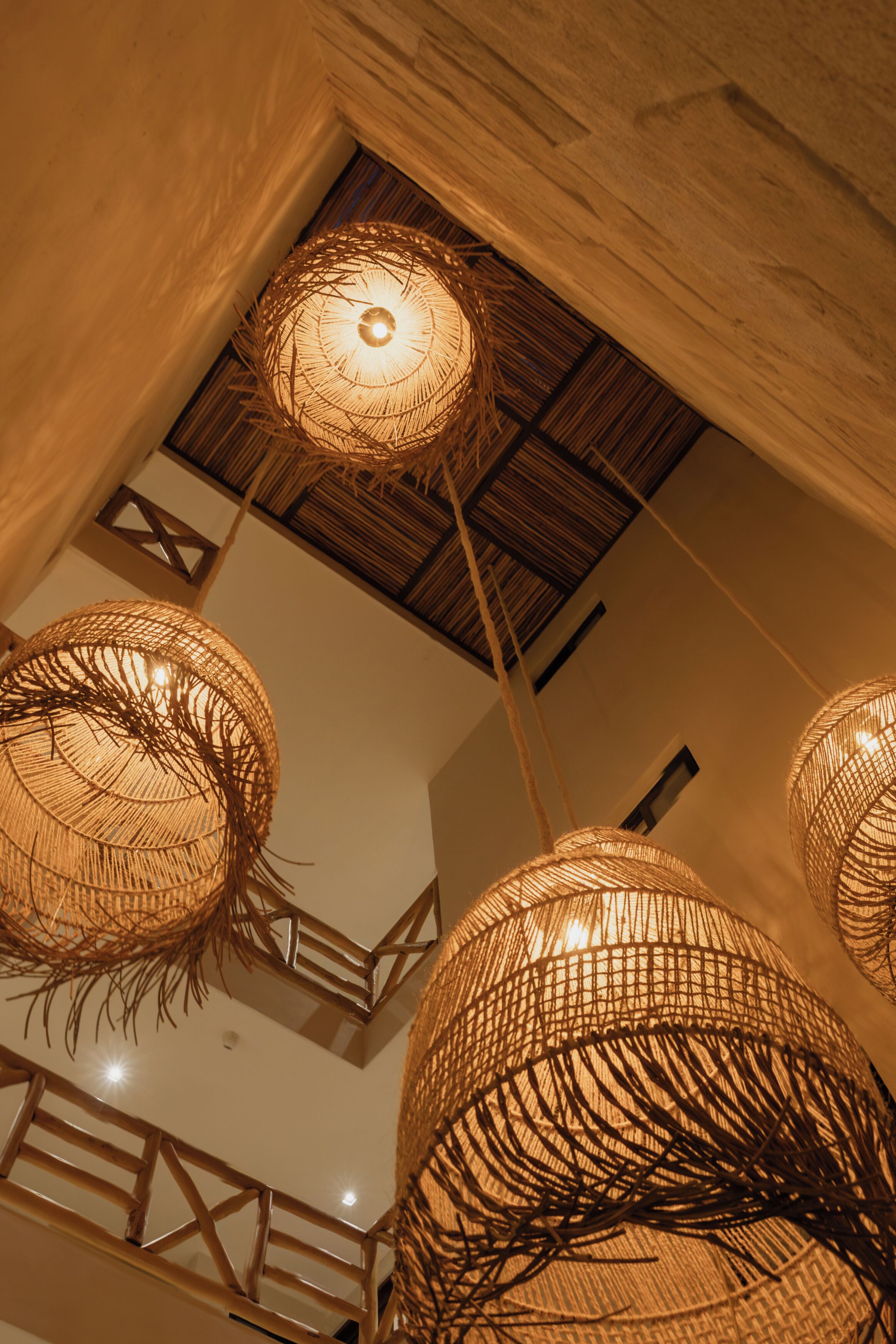 Un plafond orné de luminaires tressés et un escalier en bois.