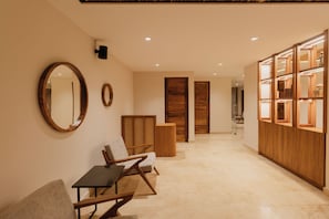 A hallway with a wooden reception desk, a seating area with chairs, and a wooden wardrobe with glass doors. - Nidara Suites (Playa del Carmen)