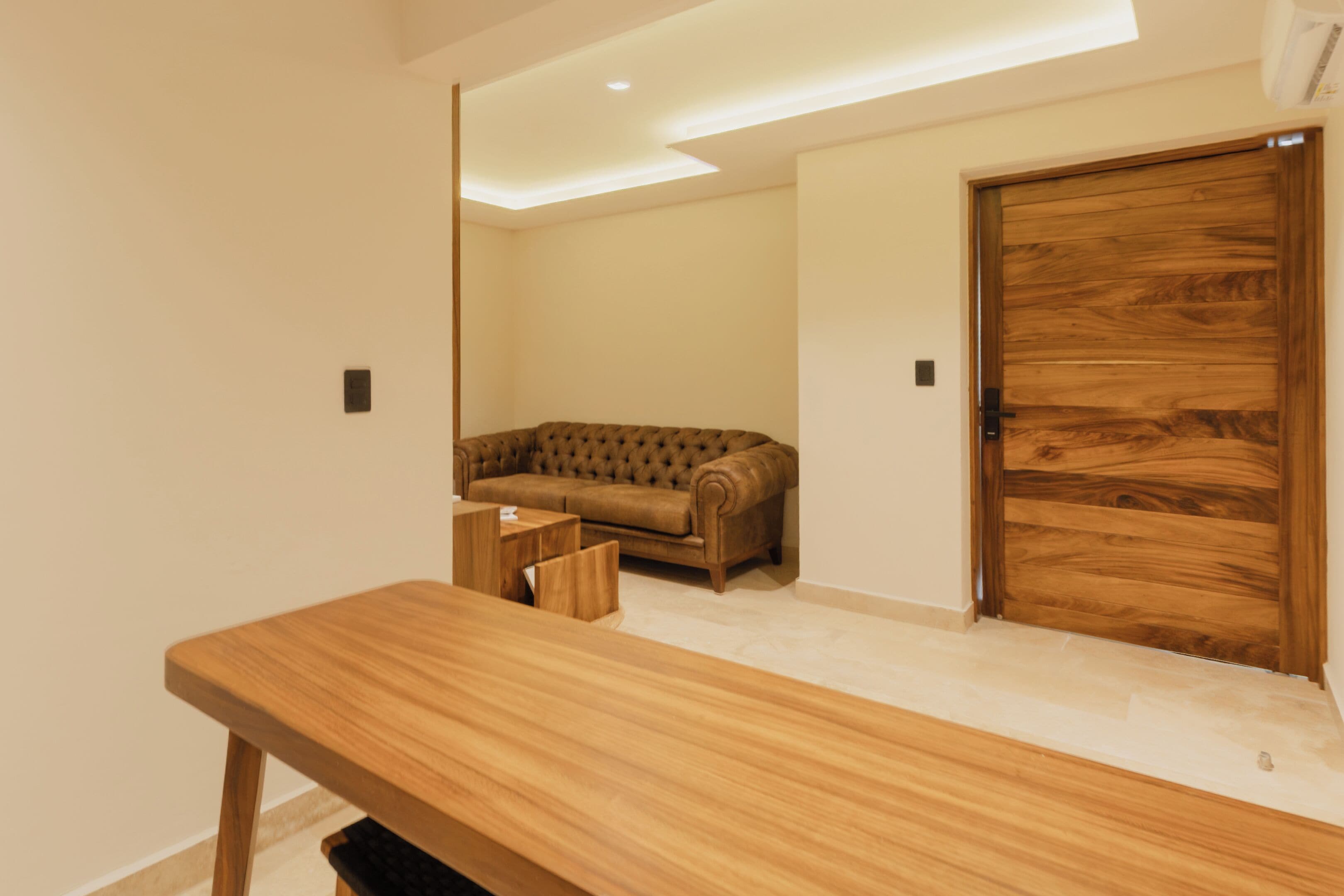 A room with a wooden desk, a tufted sofa, and a wooden door.
