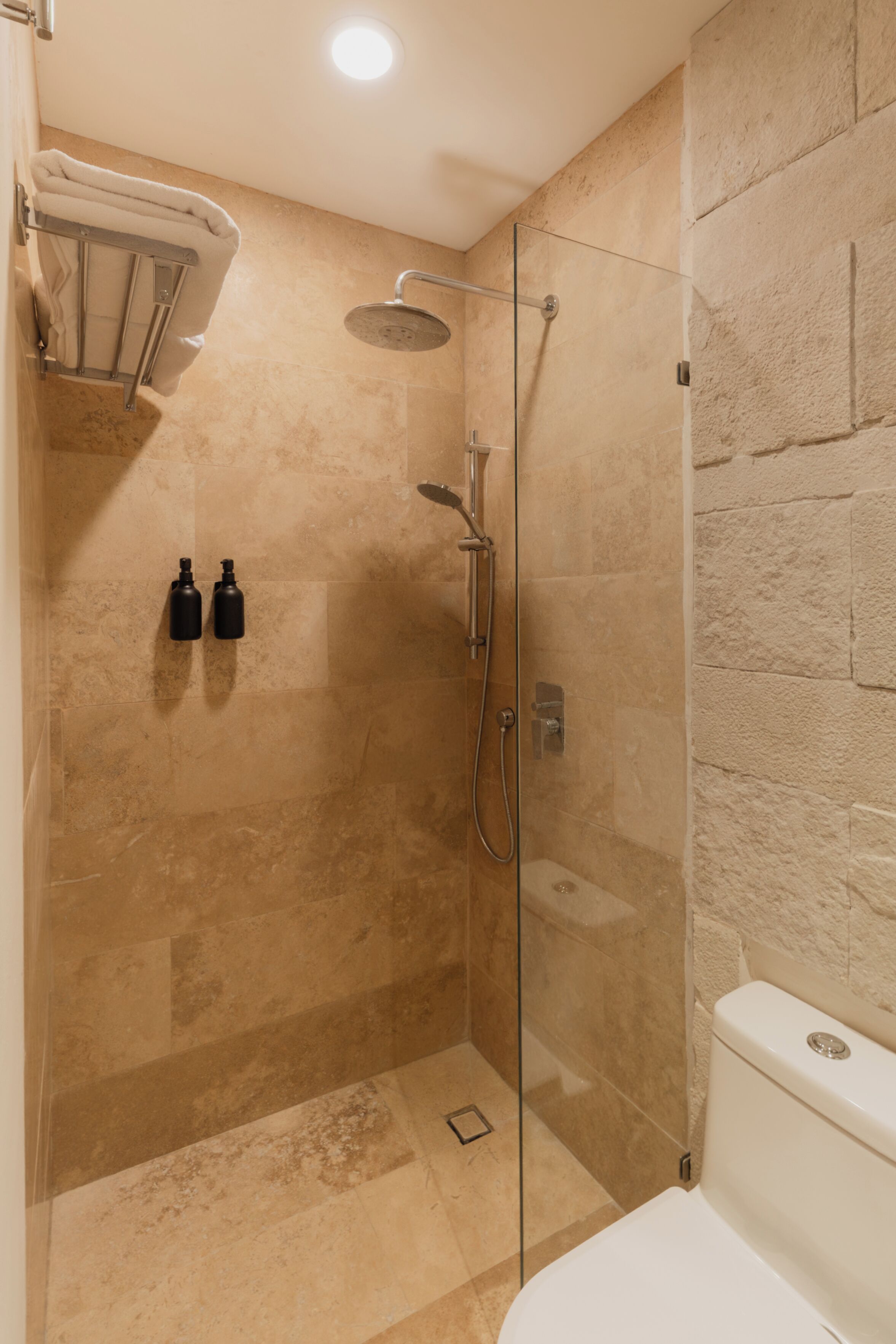Un baño moderno con cabina de ducha de vidrio, baldosas color beige y un inodoro blanco.