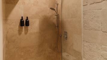 Un baño moderno con cabina de ducha de vidrio, baldosas color beige y un inodoro blanco.