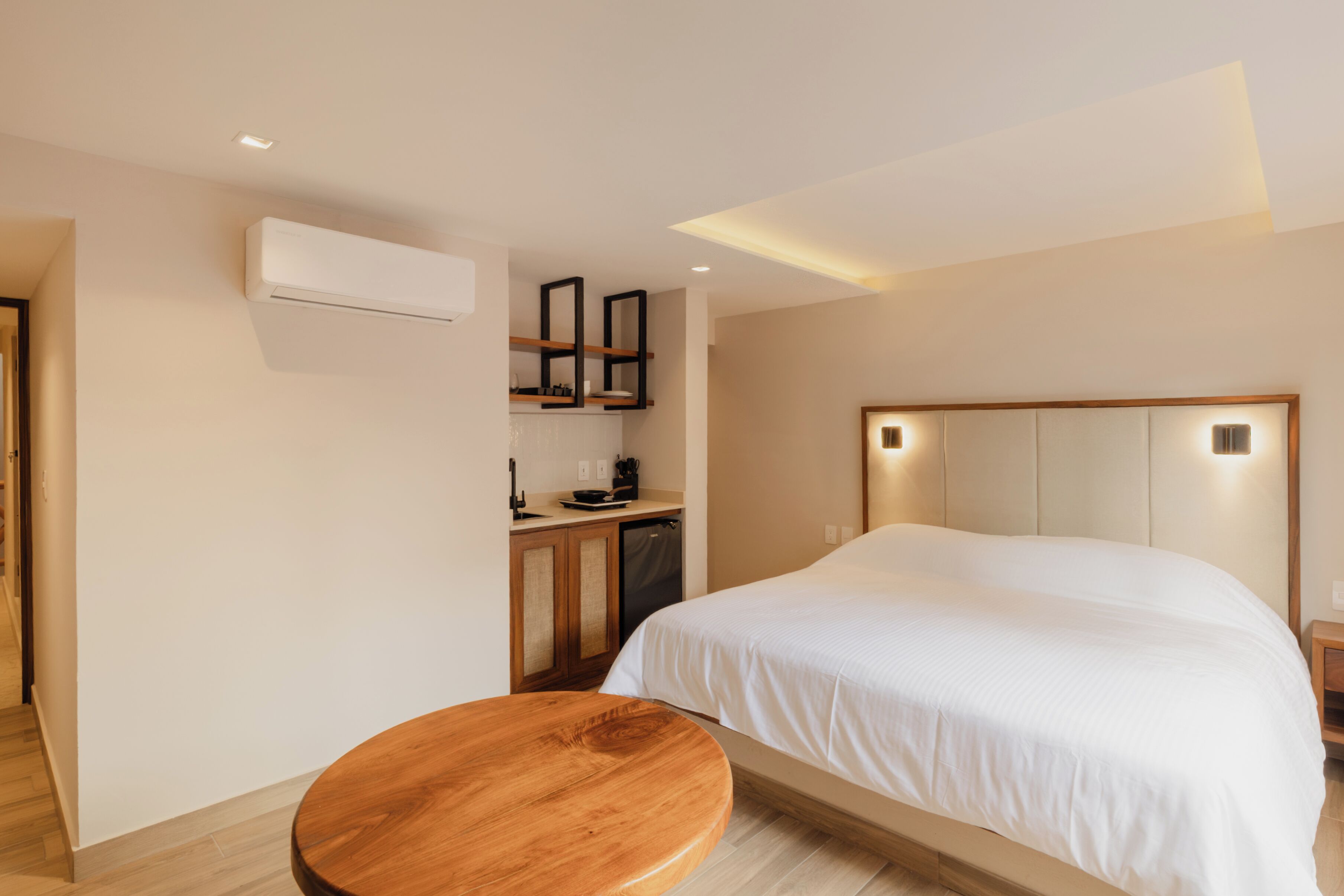 Une chambre d’hôtel moderne avec un grand lit, un tabouret en bois, un bureau intégré et un climatiseur fixé au mur.