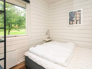 Ein Schlafzimmer mit einem Bett, einem Nachttisch, einer Lampe, einem Fenster und einem Bild an der Wand.