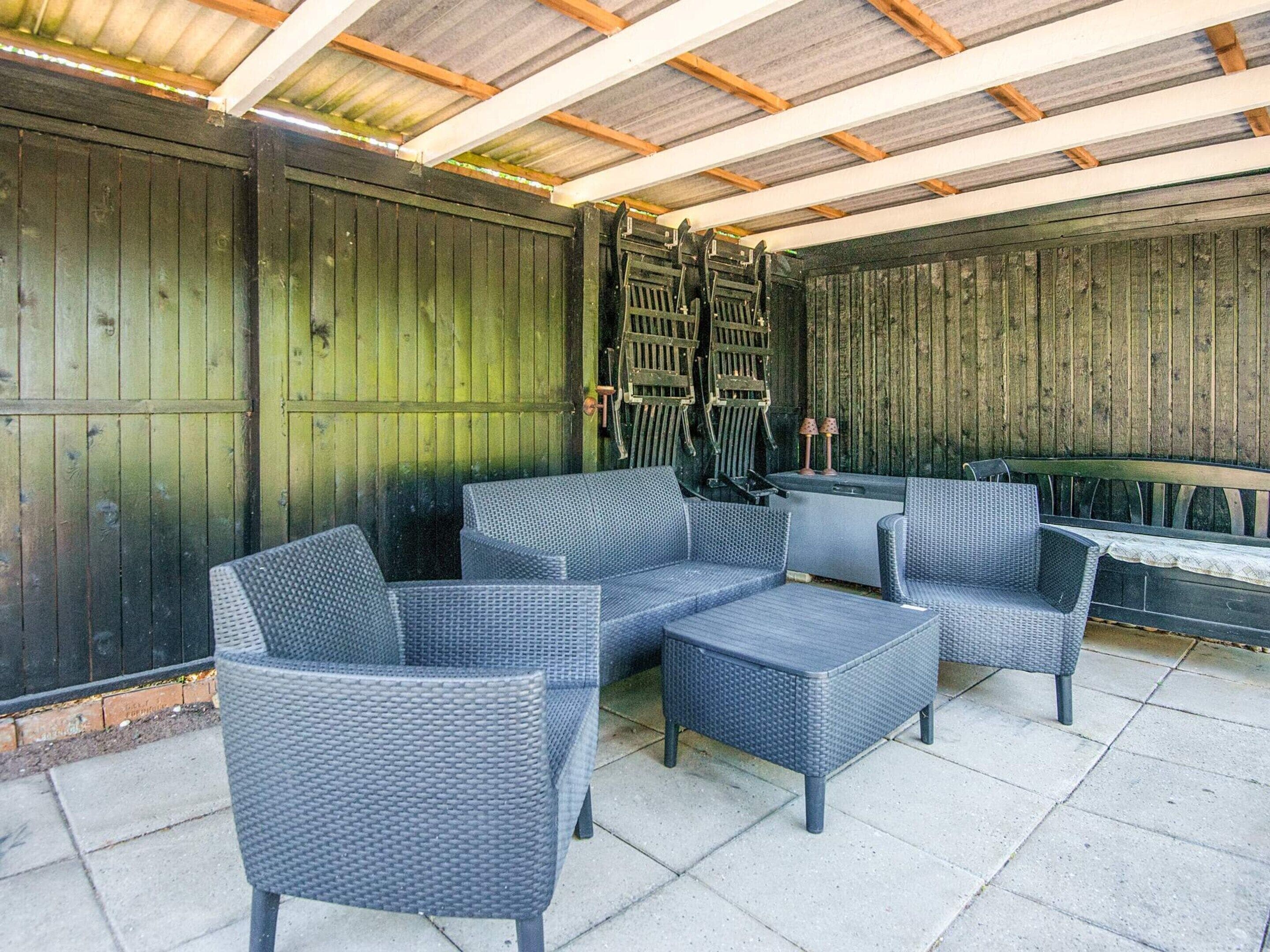 Een terras buiten met rieten meubels en een houten wand.