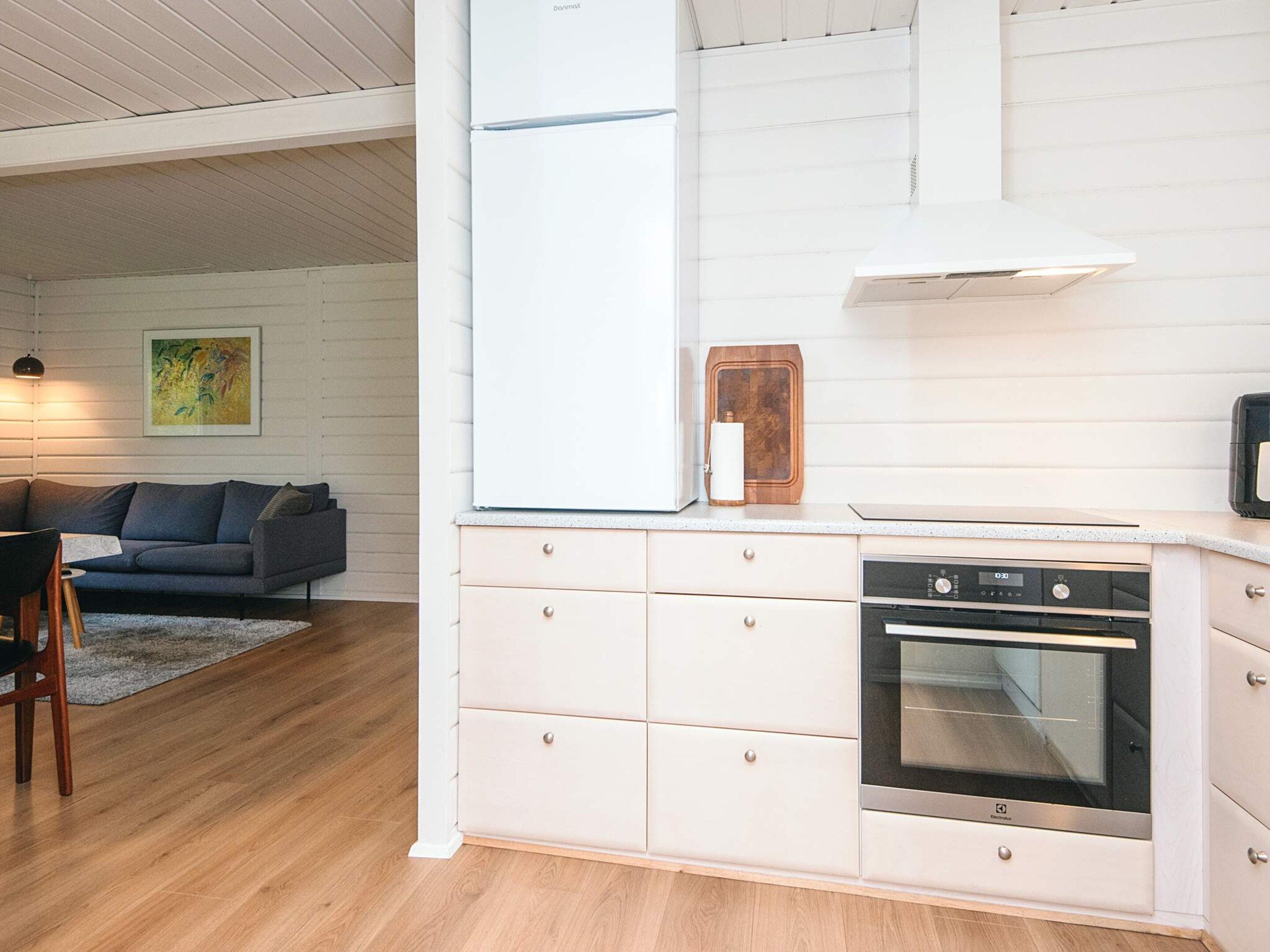 A modern kitchen with a built-in oven, a white refrigerator, and a wooden cabinet.