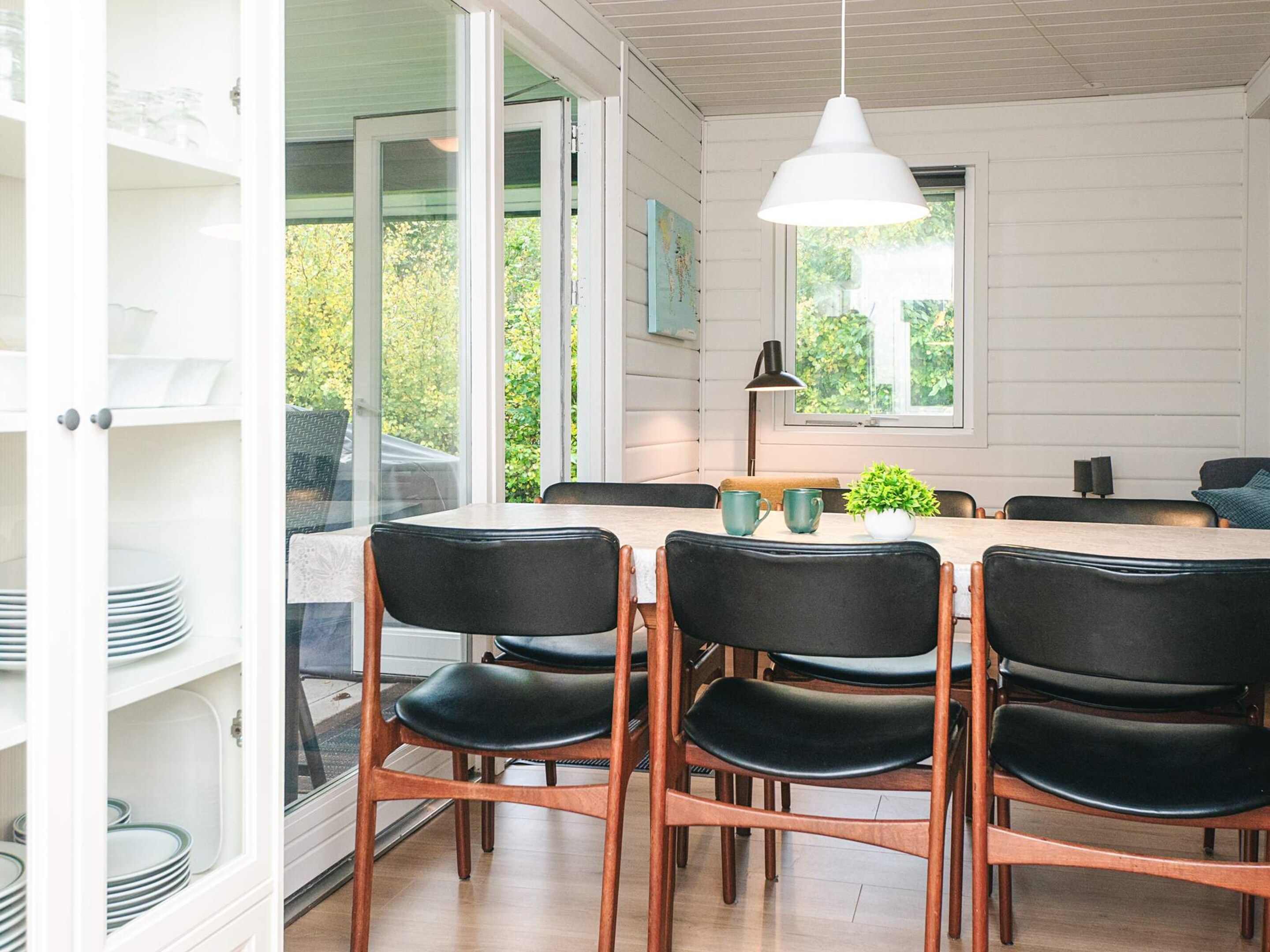 A dining area with a table and chairs, a pendant light, and a view of greenery outside.