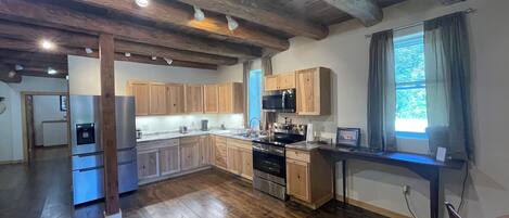 A spacious kitchen with wooden cabinets, a built-in microwave, and a large window with curtains.