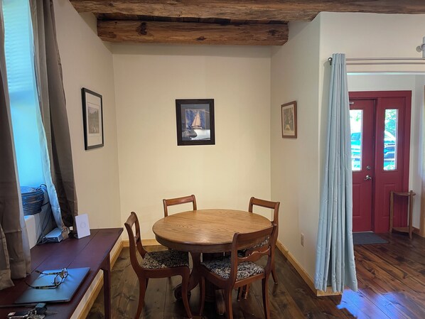 Un comedor con una mesa y sillas de madera, cuadros en la pared y una puerta roja al fondo.