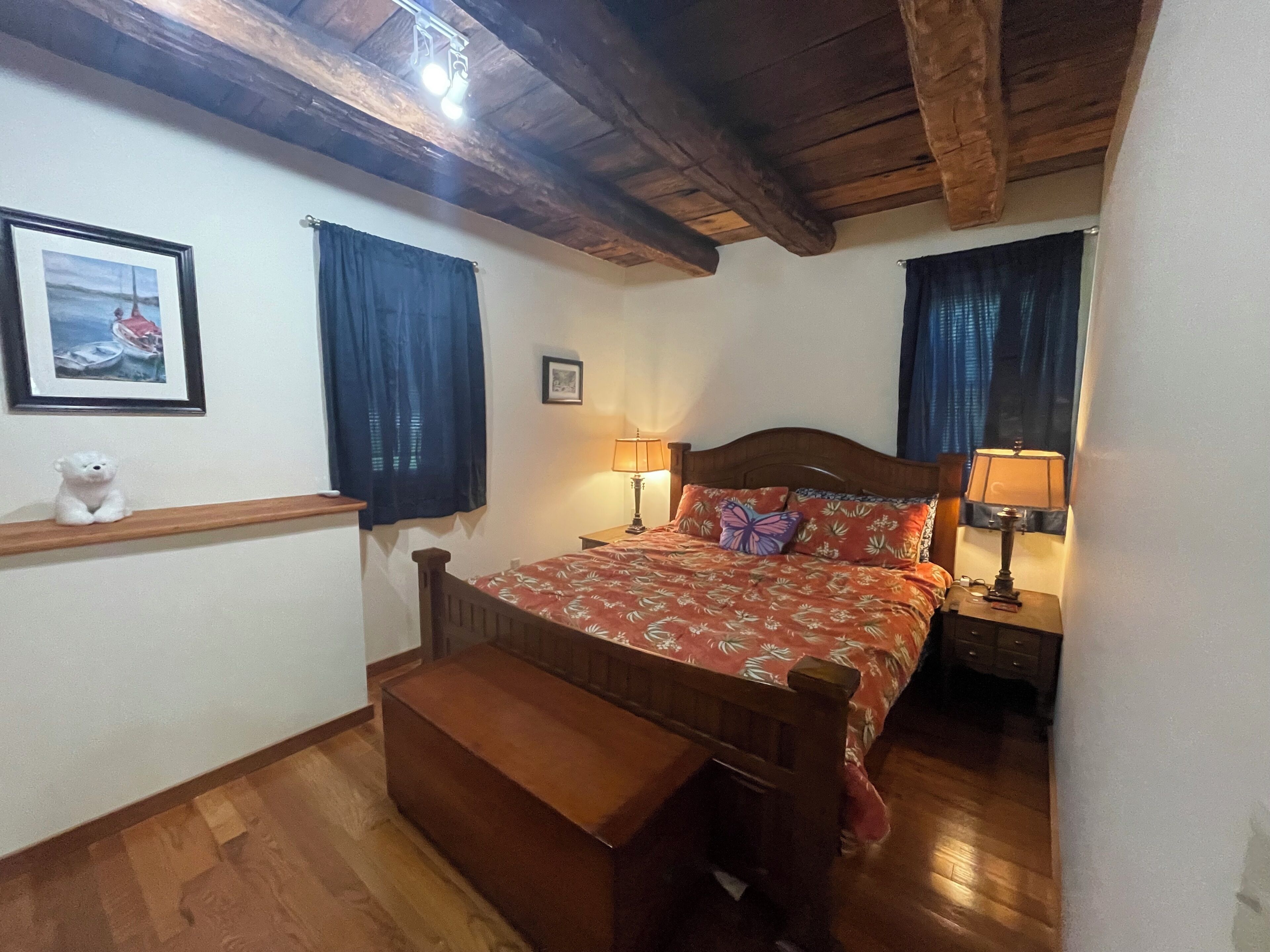Een slaapkamer met een houten bed, twee bedlampen, een houten bankje, een klein wit berenbeeldje en een lijst met een afbeelding aan de muur.