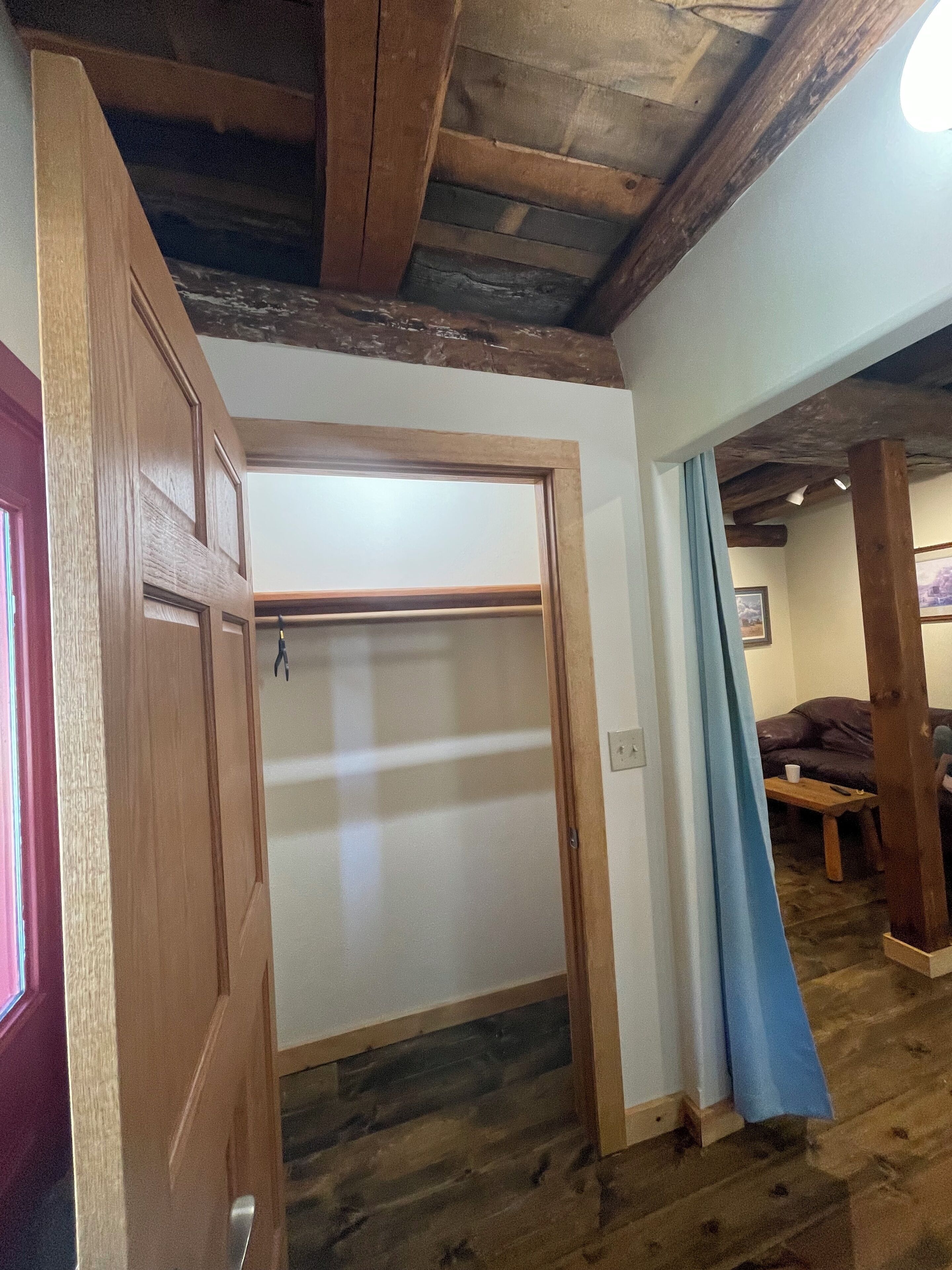 Ein Zimmer mit Holztür, Deckenbalken, einem Fenster und einer Couch.
