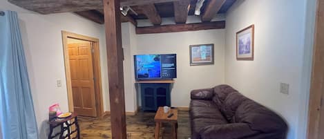 A living room with a wooden ceiling, a television, a fireplace, and a brown leather sofa.