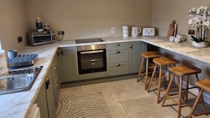 Una cocina moderna con horno empotrado, microondas, cafetera y tostadora. Hay taburetes de madera y una alfombra estampada.