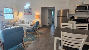 A modern kitchen with stainless steel appliances, a dining area with white chairs, and a living room with a sofa and blue armchairs. - New 4 bedroom house in Spanish Wells just steps away from the beautiful beach. (Spanish Wells)